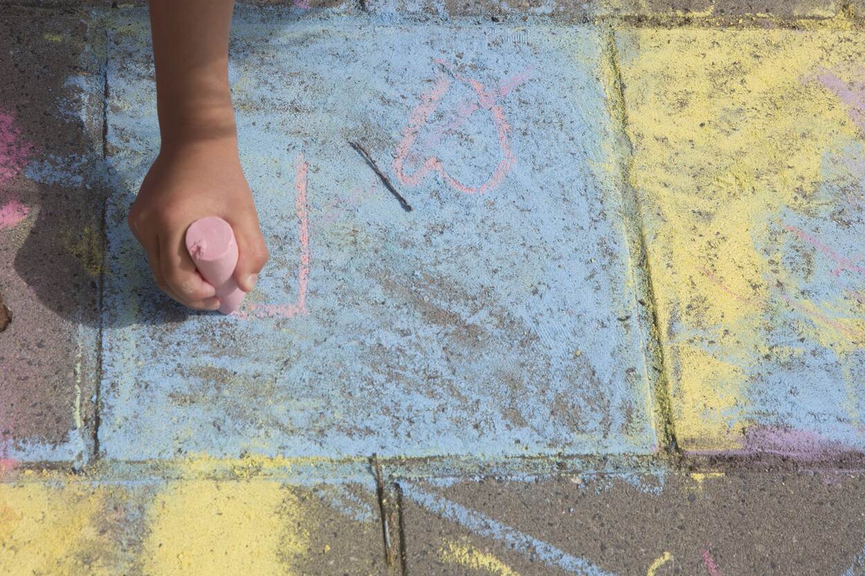 Op de stoep is gestoepkrijt. Eén stoeptegel is blauw gekleurd. Een kinderhand tekent een hartje