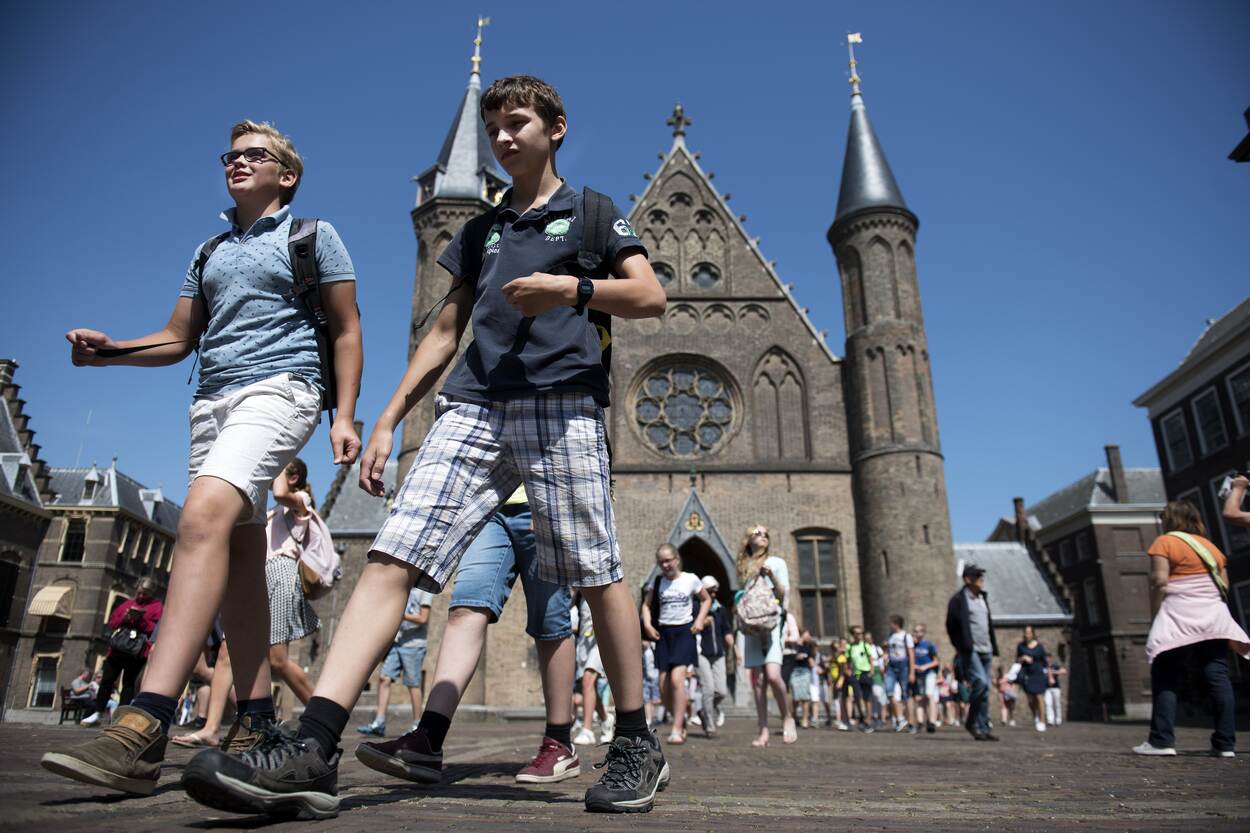 Rond de twintig kinderen lopen met hun rugzak op het Binnenhof. Zij hebben een korte broek en een t-shirt. Op de achtergrond zie je de Ridderzaal.