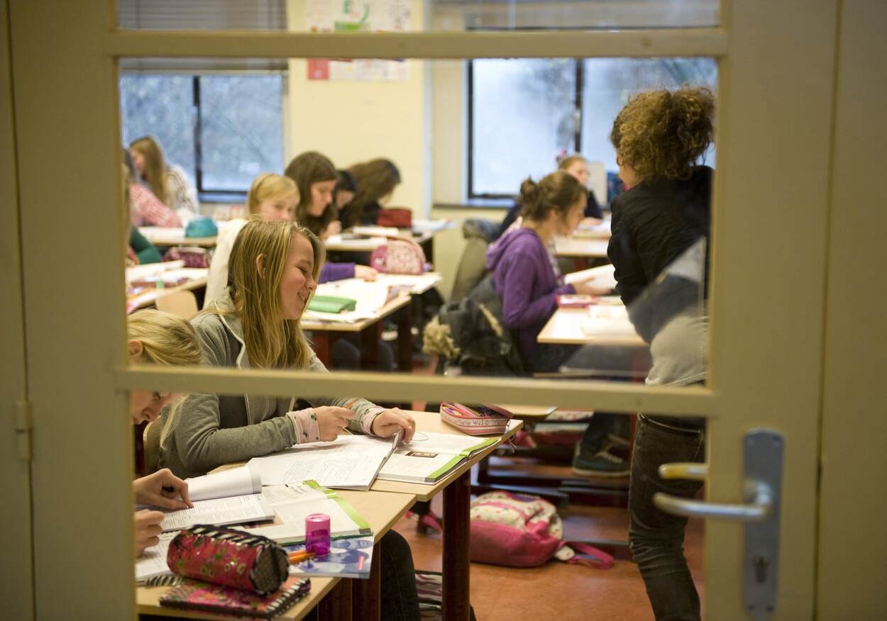 In het klaslokaal zijn meiden opdrachten aan het maken. Hun boeken en schriften liggen op tafel. De tafels staan twee aan twee opgesteld.