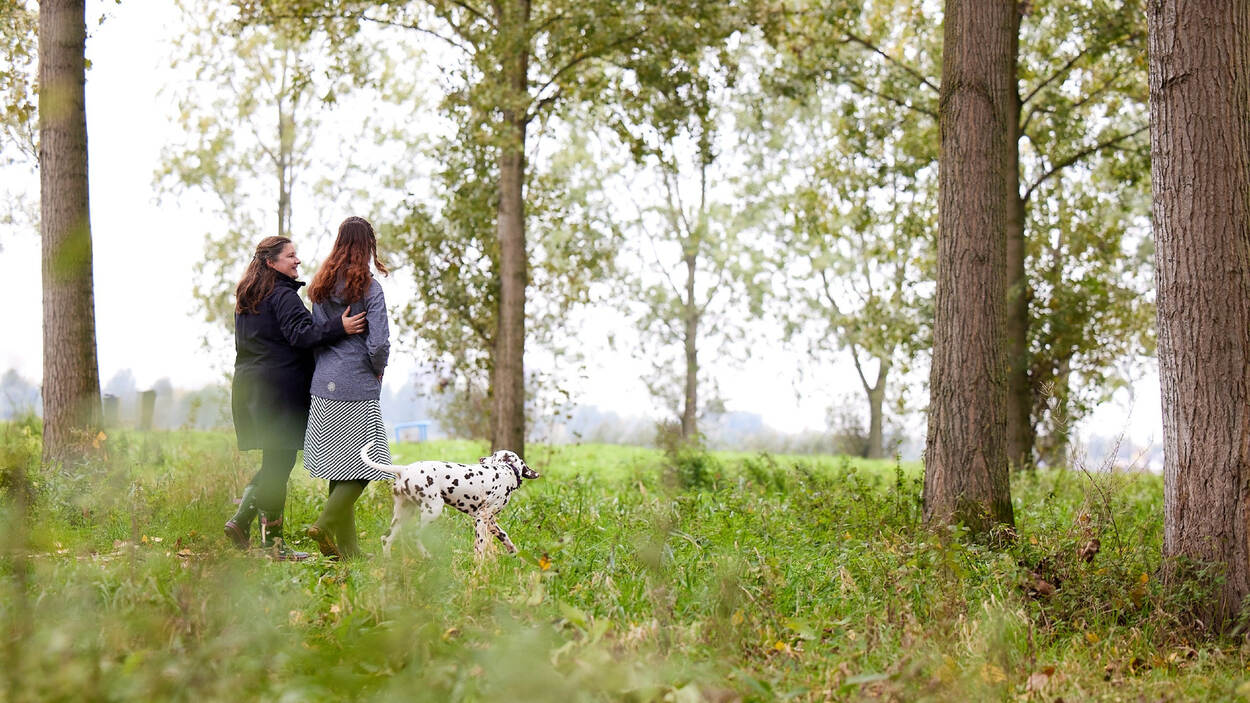 Twee vrouwen in het bos met een hond. De ene vrouw heeft een arm geslagen om de ander