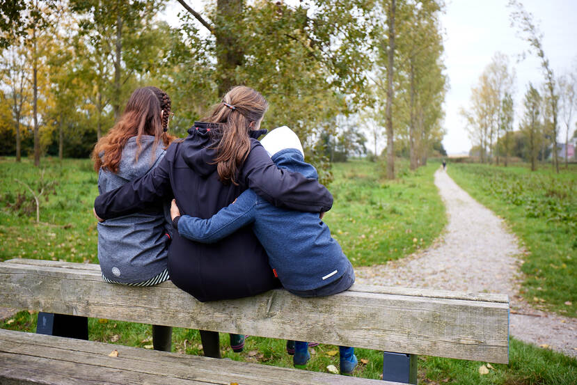 Drie jongeren zitten op een hekje en omhelzen elkaar.