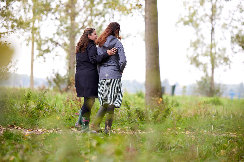 Twee vrouwen wandelen. De een omhelst de ander.