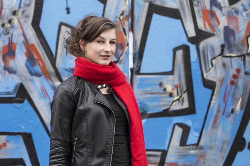 Meisje met een rode sjaal staat voor een graffiti muur