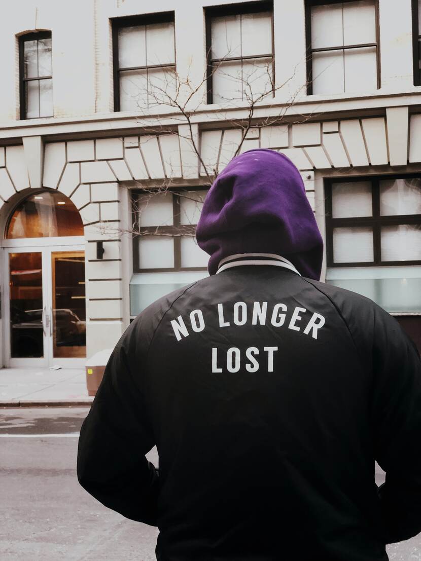 Een jongere die een jack draagt met de woorden "no longer lost" staart naar een gebouw met de rug naar de camera gekeerd.