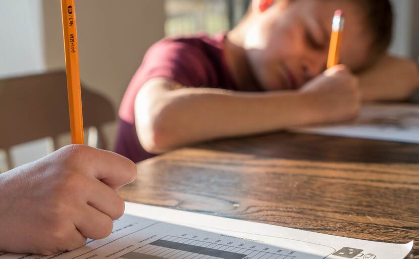 Jongen aan tafel die met een potlood schrijft op een papier