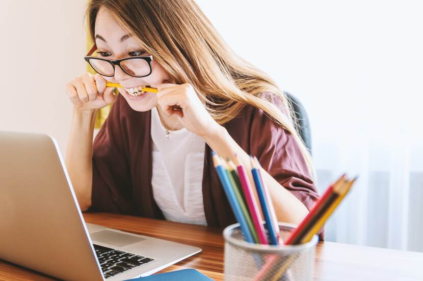 Aziatische vrouw zit voor laptop en bijt op potlood