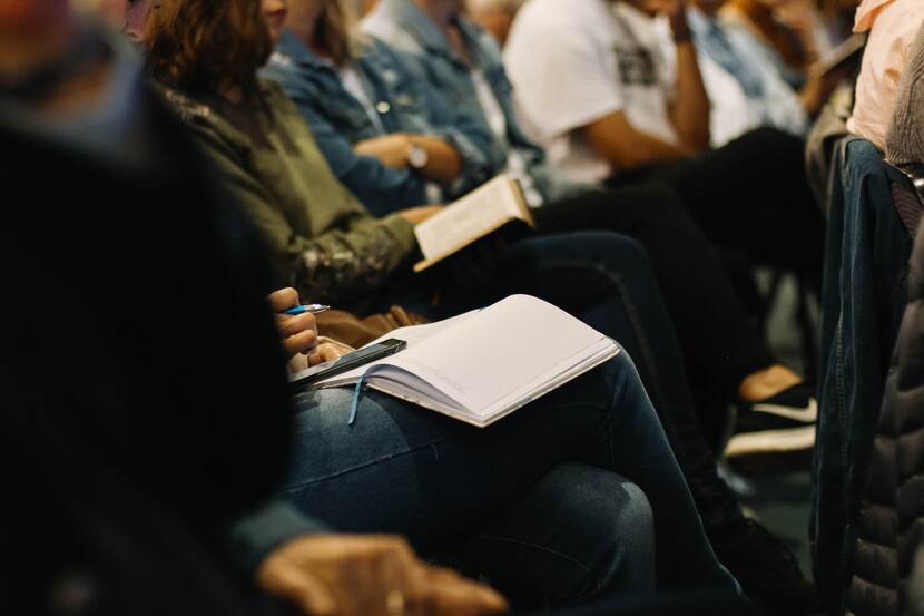 Mensen wonen een seminar bij. Twee personen hebben een aantekeningboek op hun schoot.